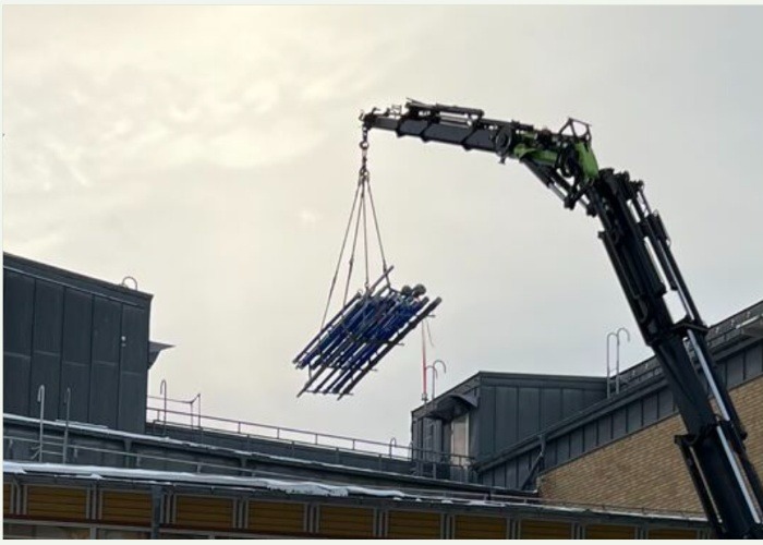 Kranbil lyfter en rörkassett upp på ett tak